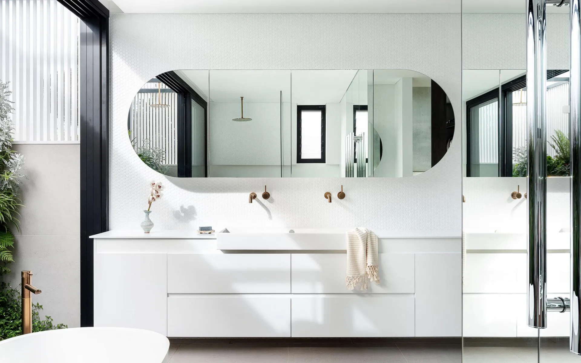 Modern white bathroom interior with sleek white vanity, large oval mirror, and textured wall tiles.