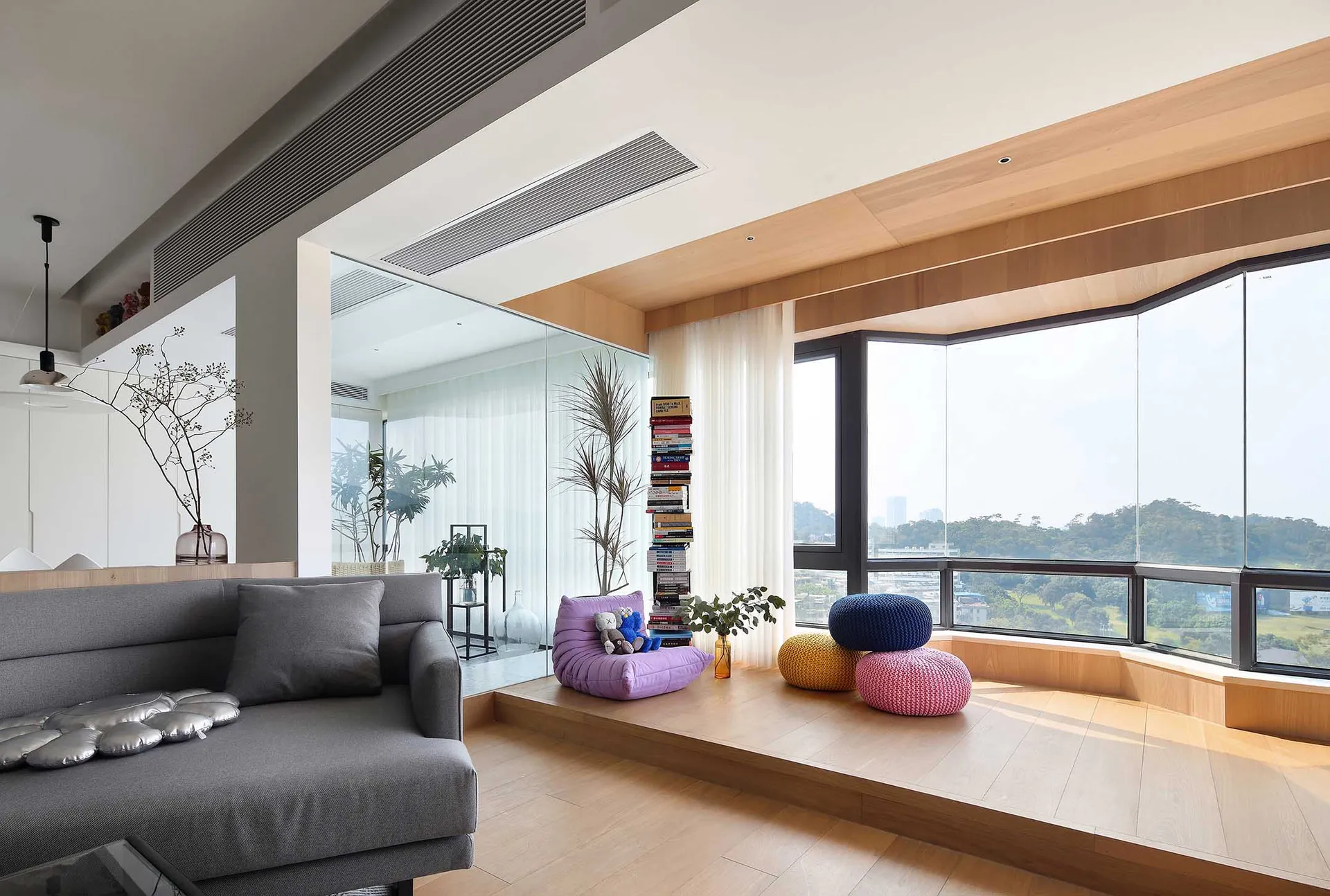 A minimalist living room featuring wooden flooring, glass walls, and fabric furniture.