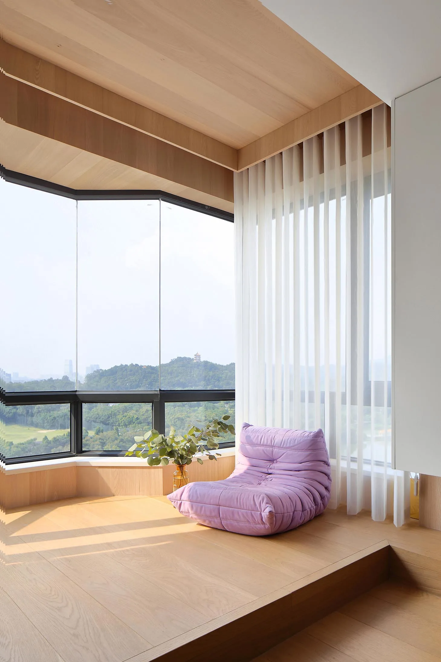 Modern window seat with a purple cushion and green plants, framed by large windows and wooden flooring.