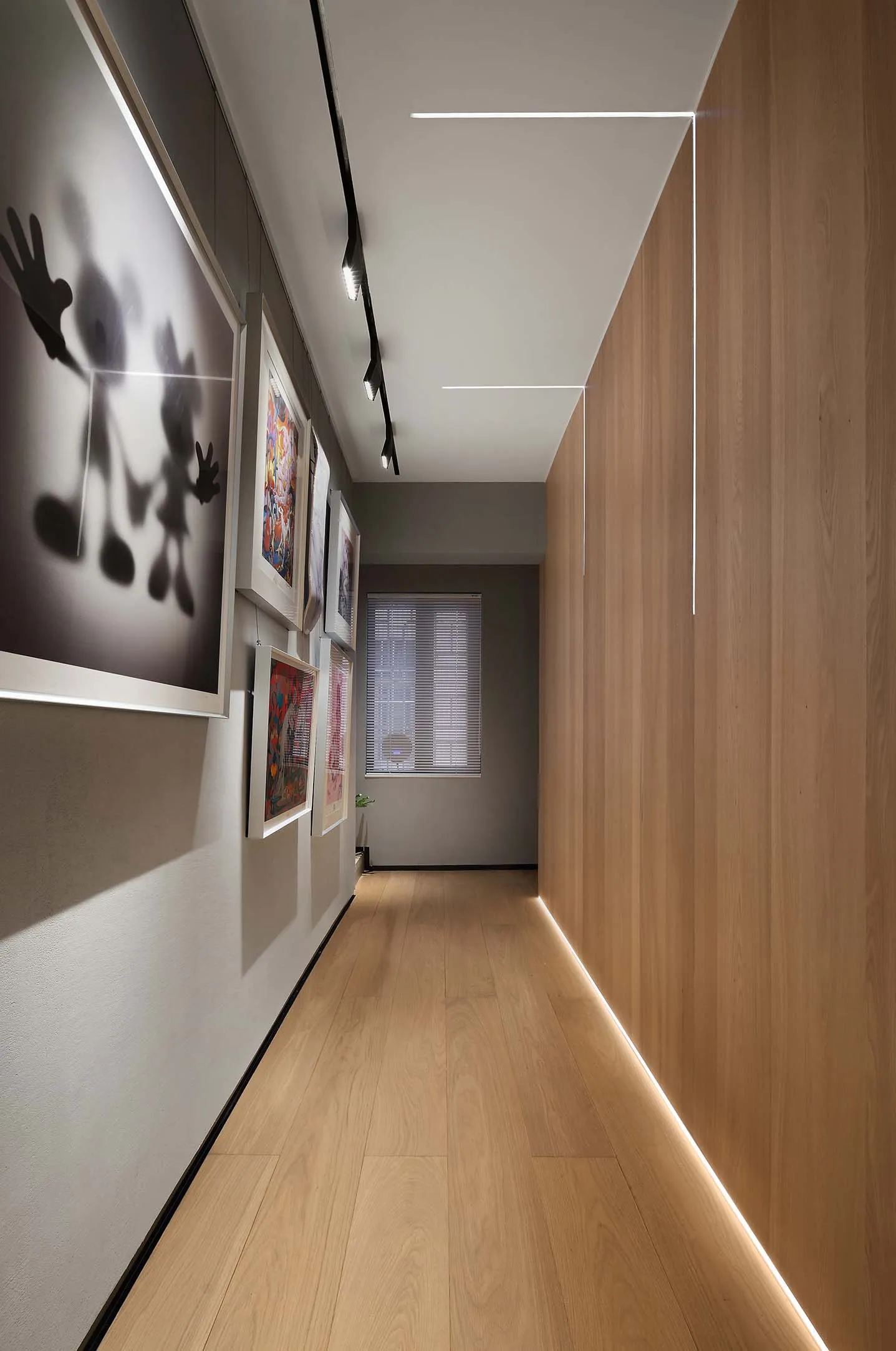 Long corridor with modern lighting fixtures, framed art, and wooden flooring.
