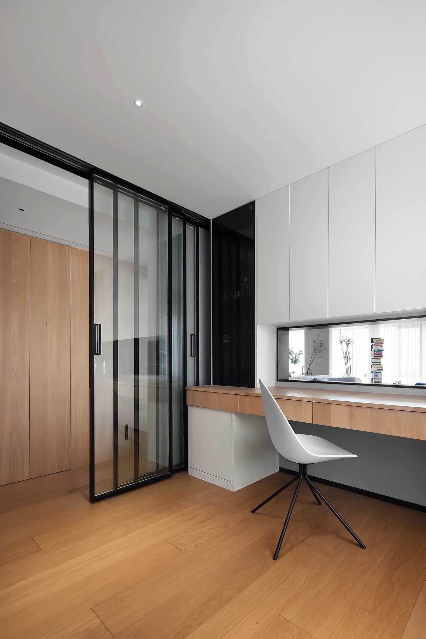 Modern minimalist home office featuring a wooden desk and chair, with integrated storage and sleek design elements.