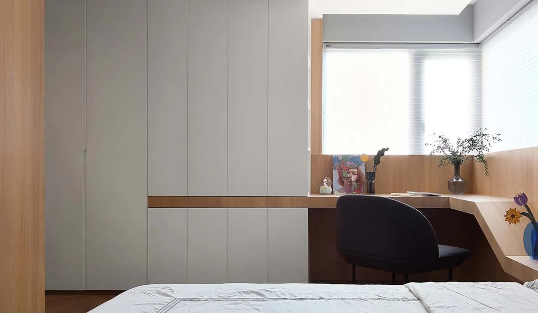 A minimalist bedroom featuring a bed, a desk with a chair, a window, and wood-paneled walls and cabinets.
