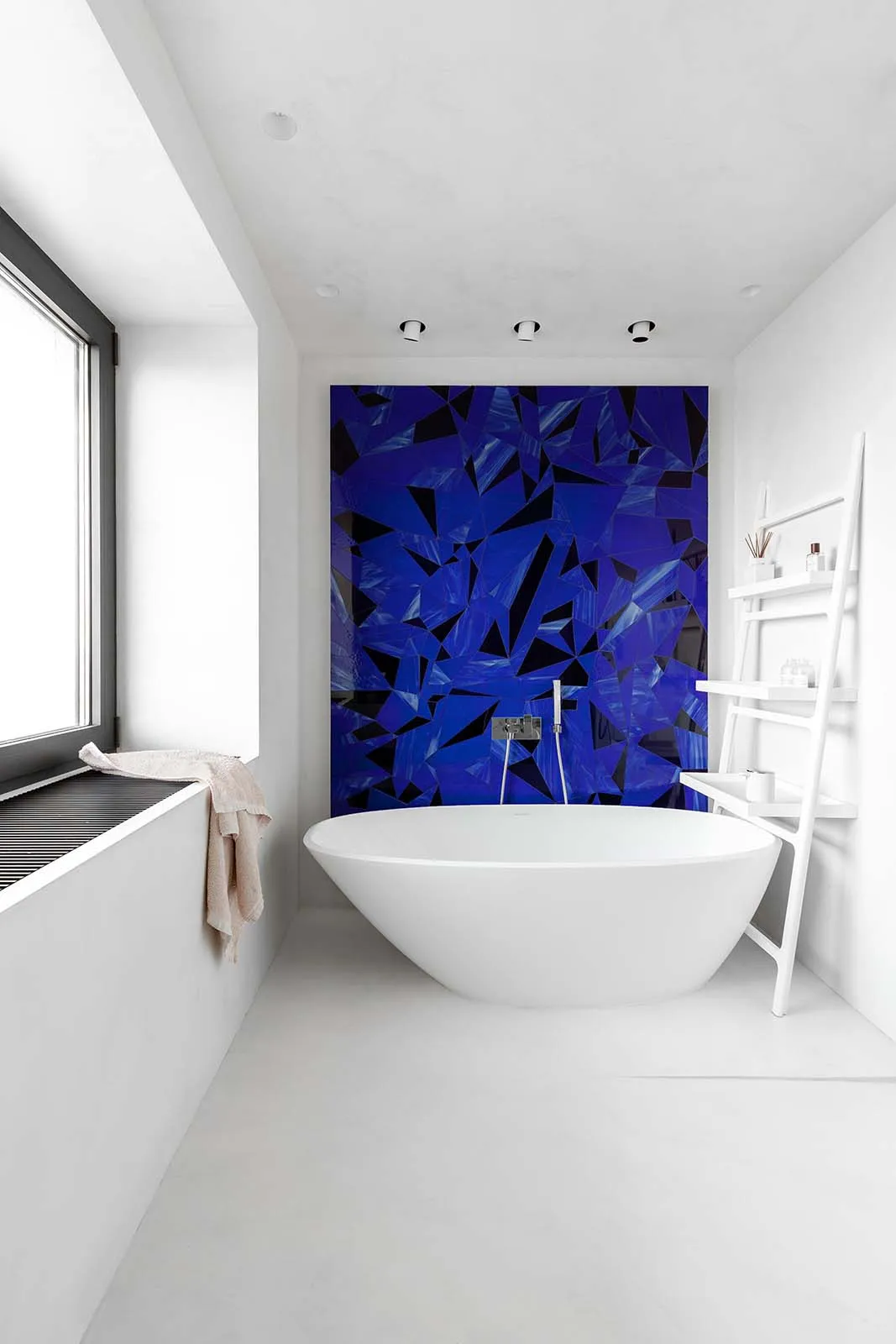 Modern bathroom with blue mosaic accent wall and white freestanding tub.