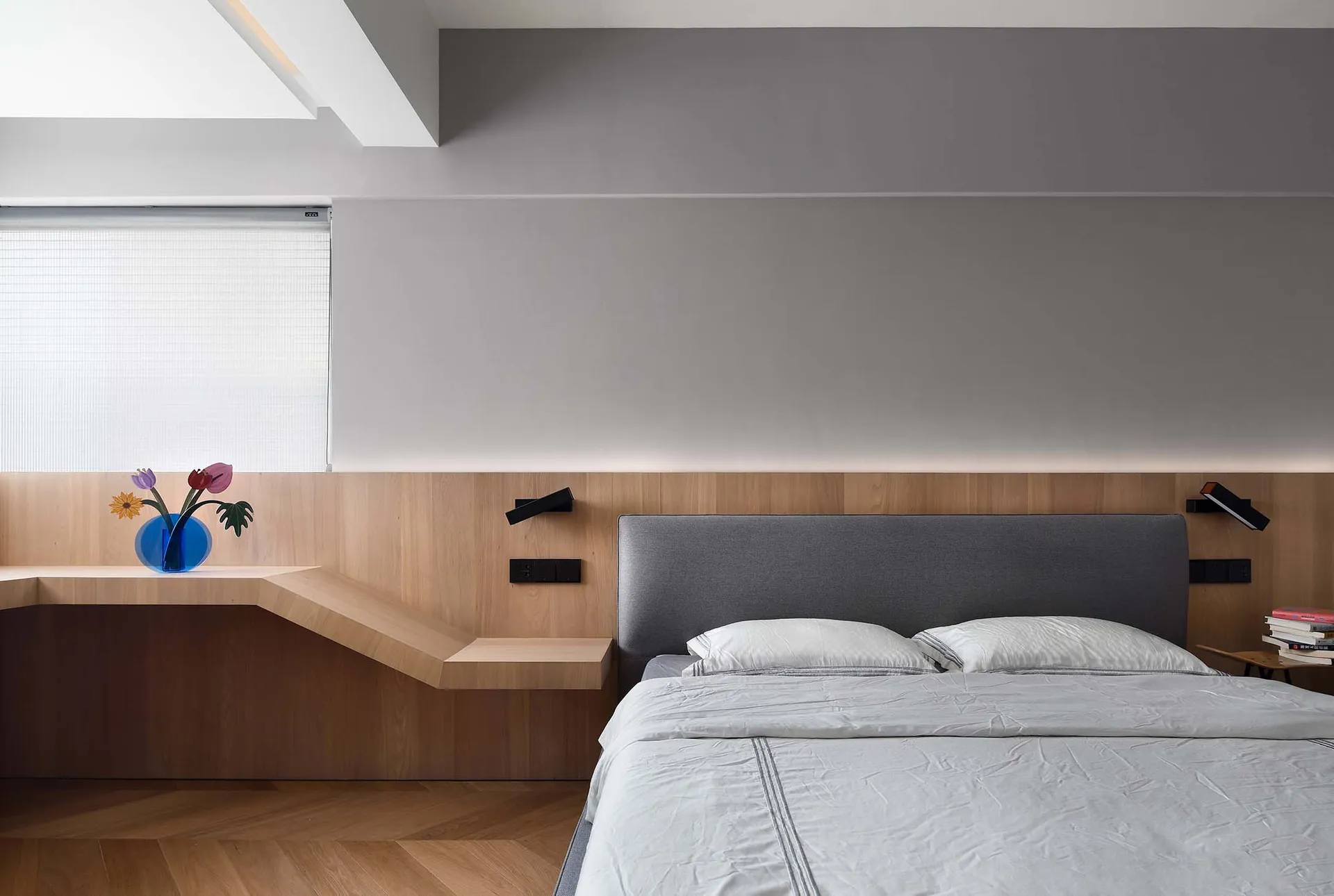 Minimalist bedroom with wooden furniture, grey headboard, and grey bedding