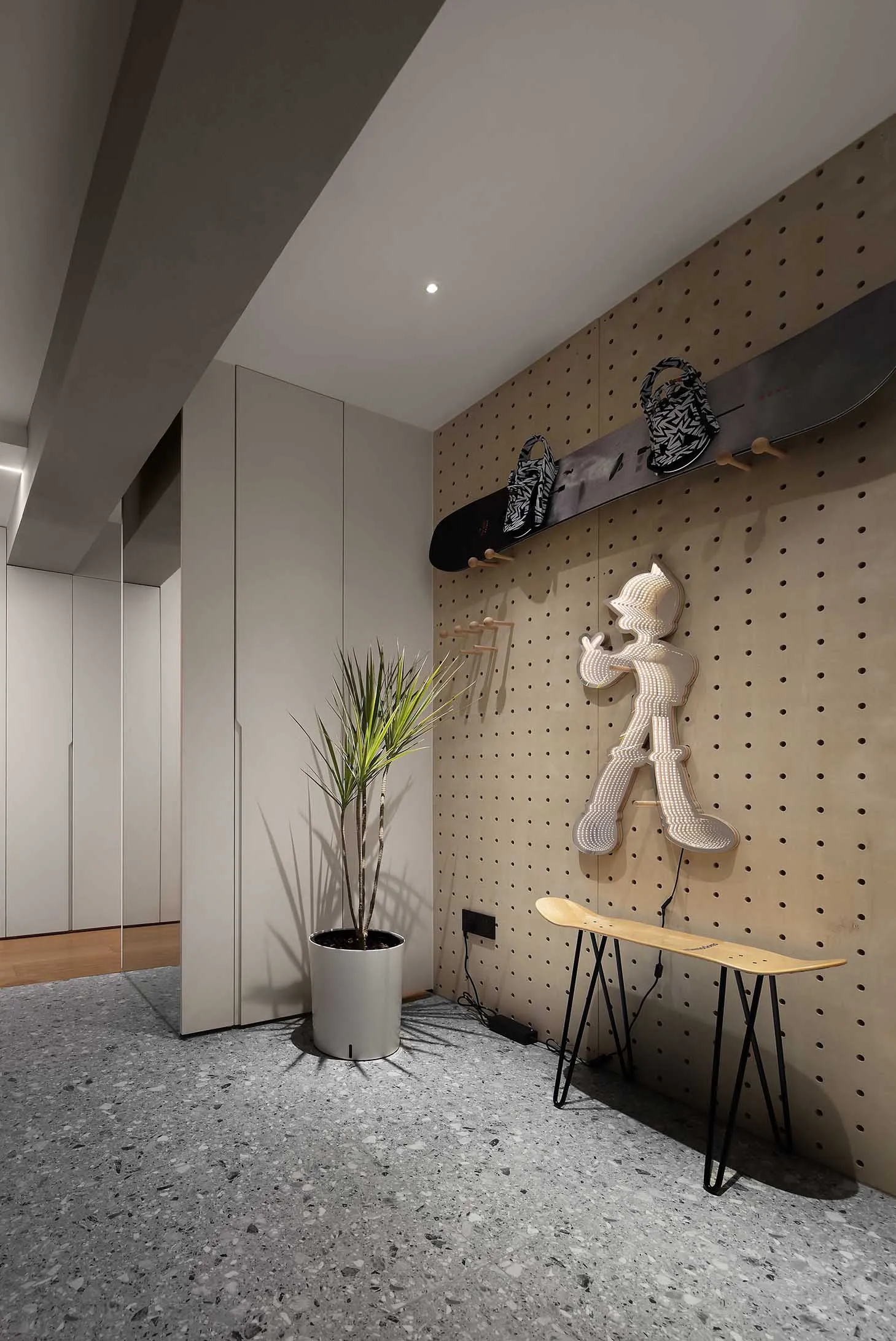A modern entryway with wood pegboard, skateboard, and plant.