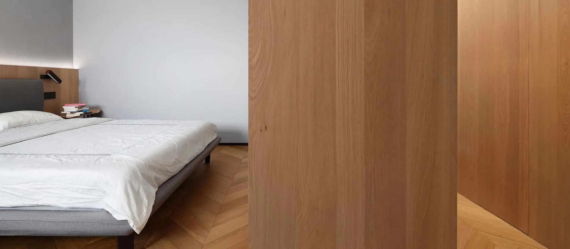A minimalist bedroom with wooden walls and a neatly made bed.