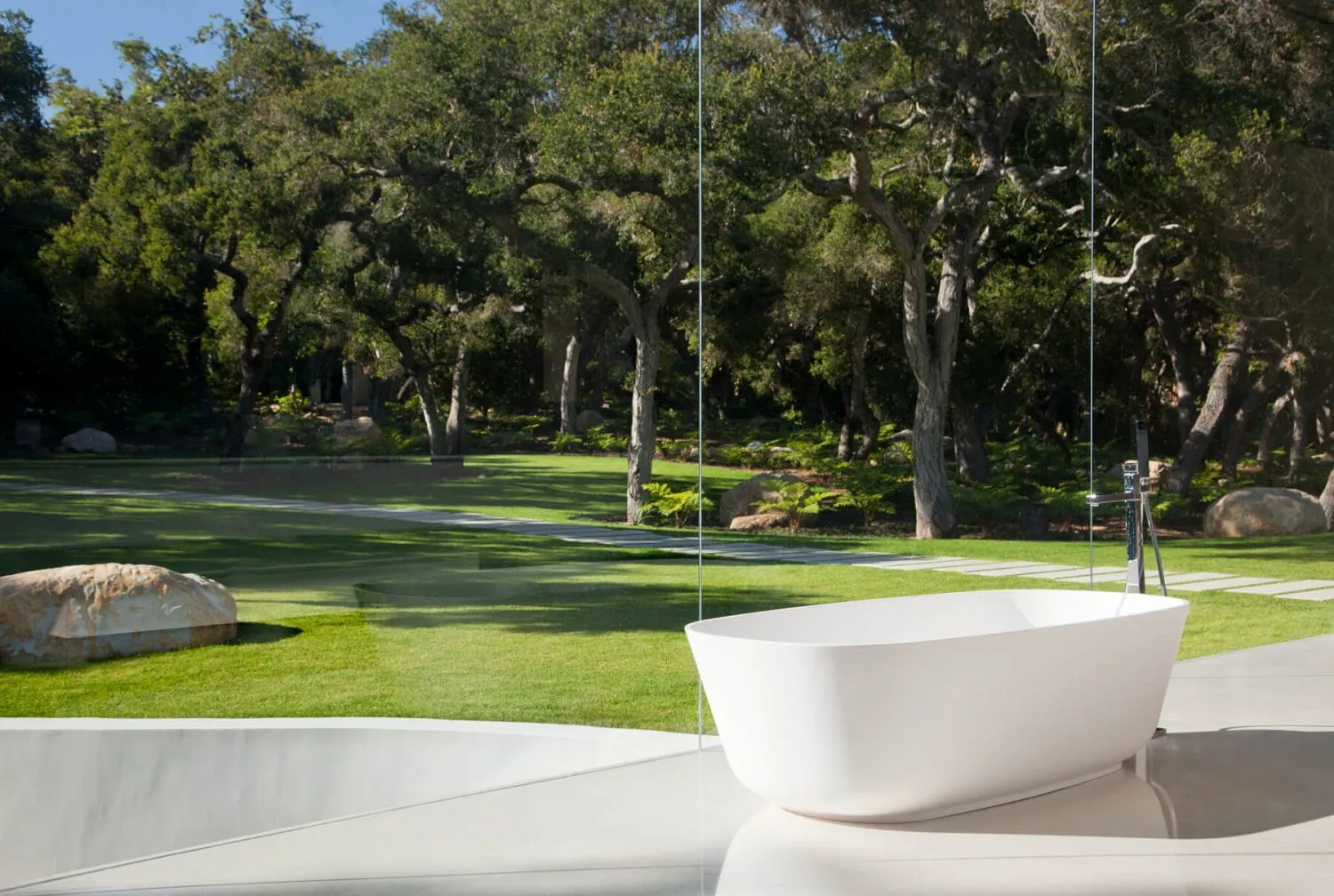 Modern, minimalist outdoor bathroom featuring a concrete bathtub and polished floor, surrounded by lush greenery and trees.