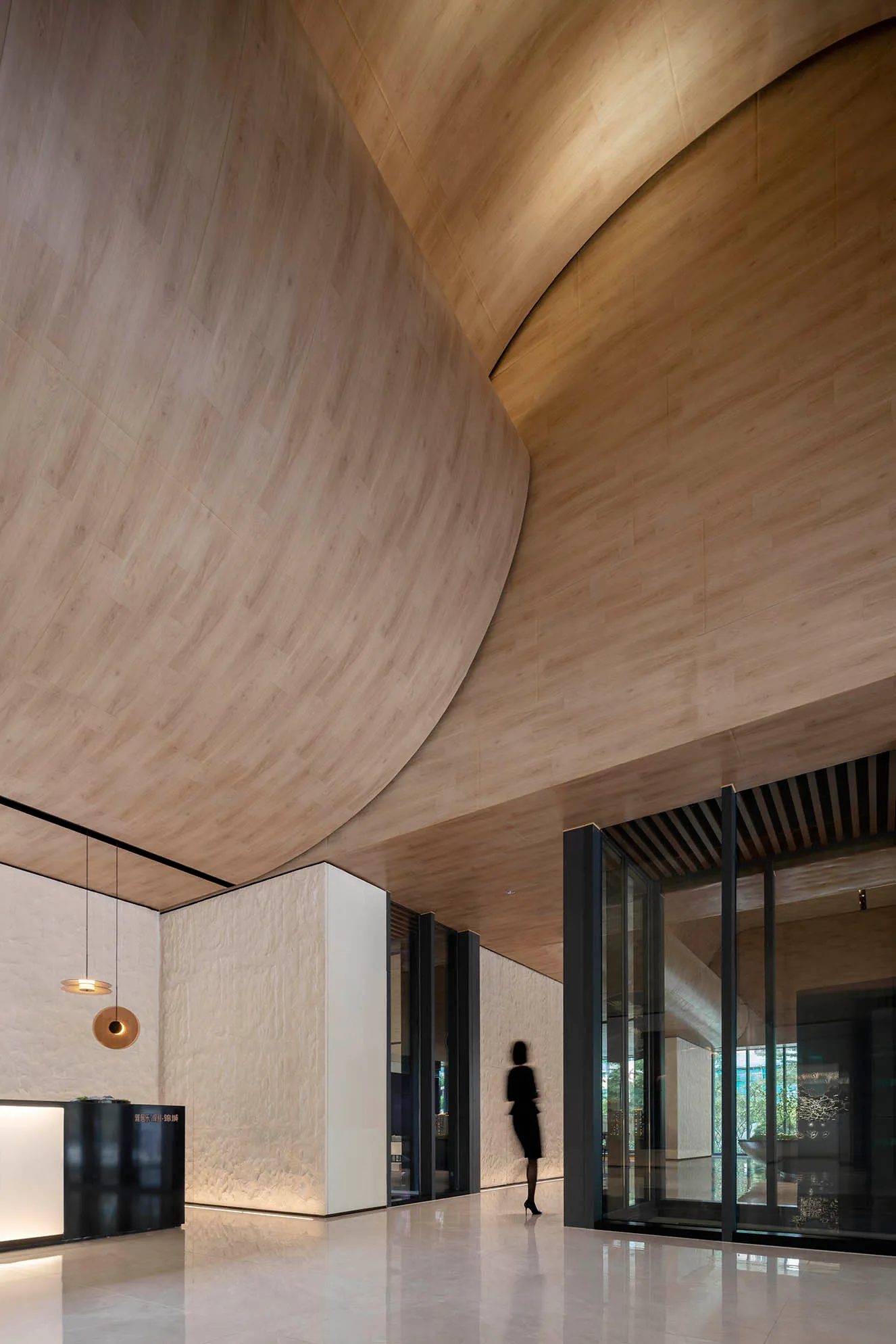 A modern hotel lobby featuring a wooden archway and marble flooring.