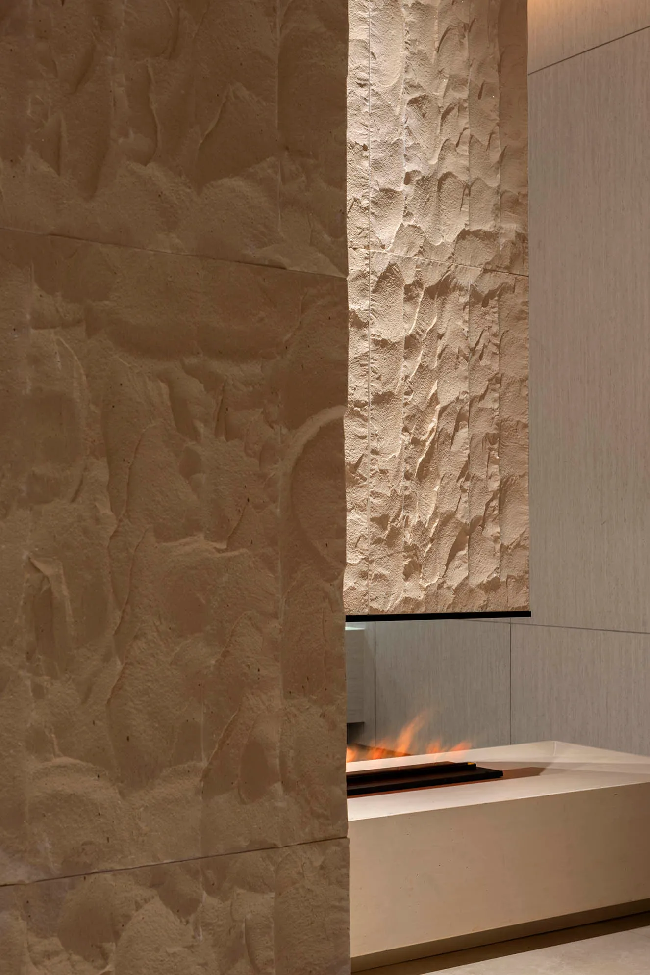 A modern minimalist fireplace with concrete walls and a fire burning inside.