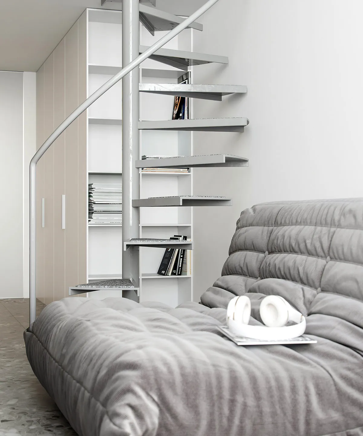 A minimalist apartment with a metal staircase, wooden floors, and a upholstered sofa.