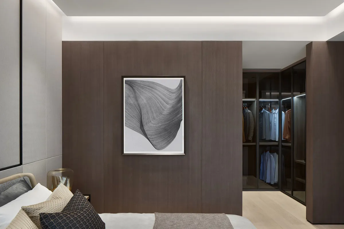 A modern bedroom featuring dark wood paneling, a bed with multiple pillows, and a walk-in closet with clothes hanging.
