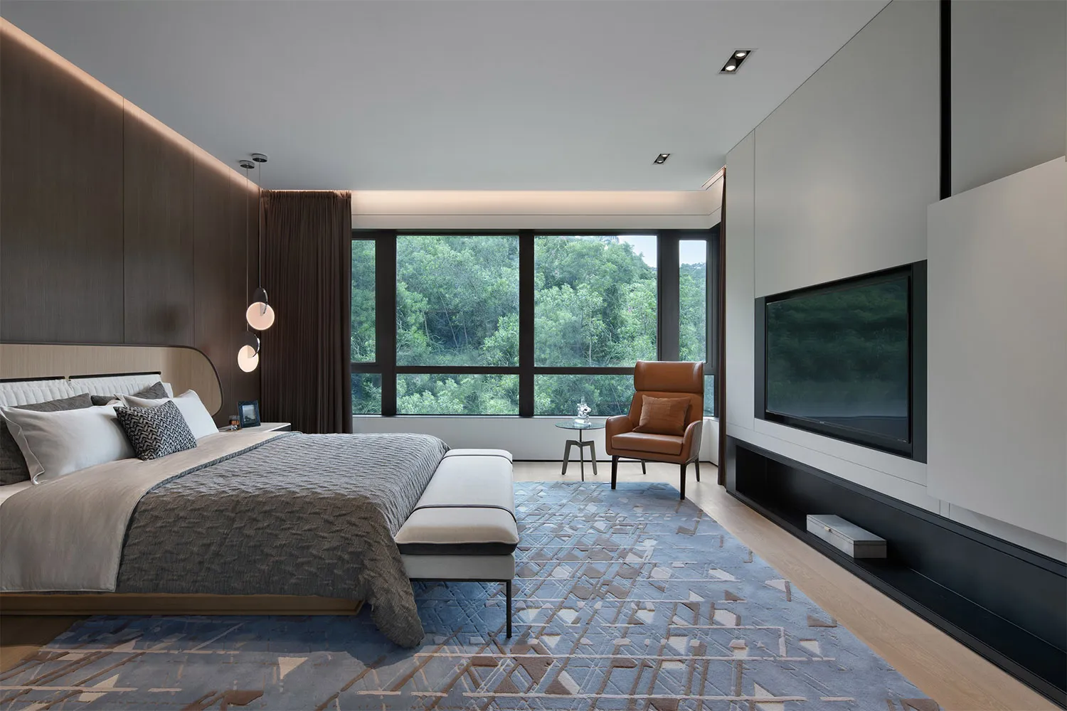 A modern, minimalist bedroom featuring a large bed with a wooden headboard, a matching bench, a leather chair, and a TV mount