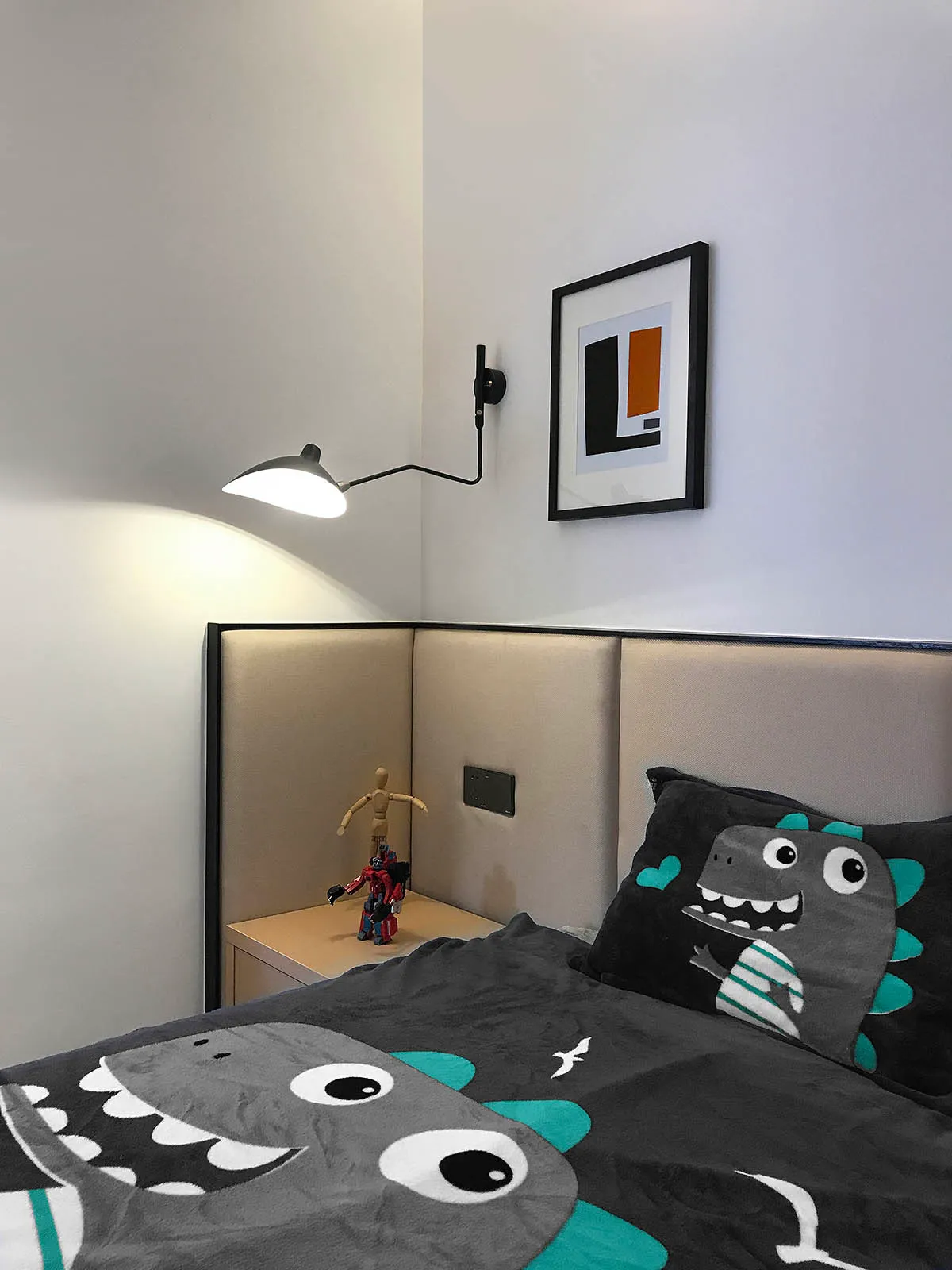 Modern minimalist bedroom with a bed featuring a dinosaur-themed quilt and a dinosaur-themed pillow, a nightstand with a Tran