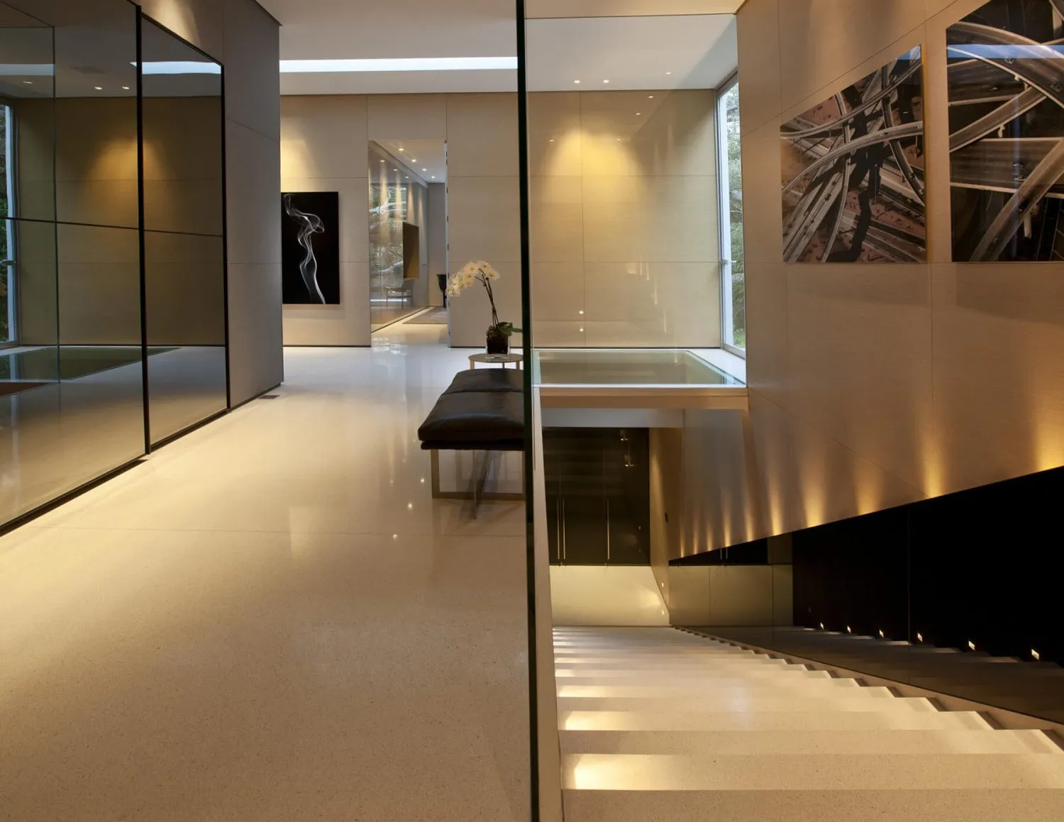 Modern minimalist interior with a glass staircase, white flooring, and minimalist decor.