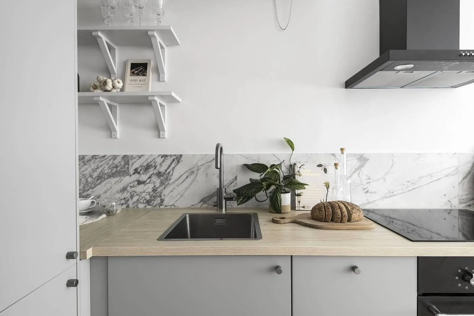 Minimalist kitchen featuring a marble backsplash and wooden countertop with a bread loaf and cutting board on the counter.