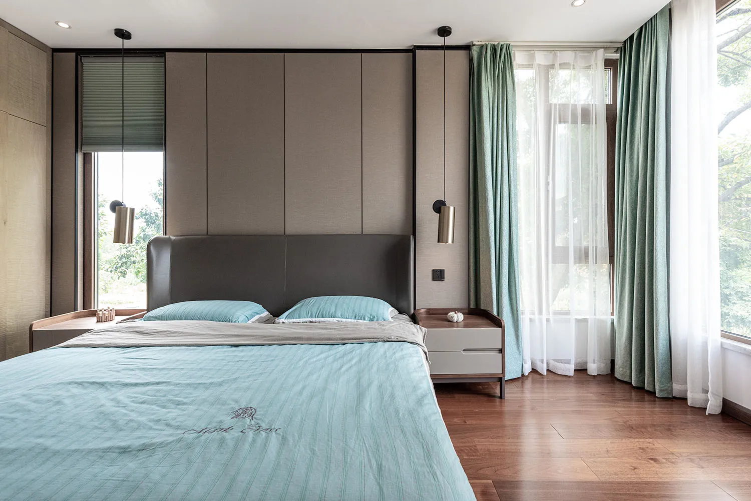 A contemporary minimalist bedroom with a grey leather headboard, blue bedding, and green curtains.