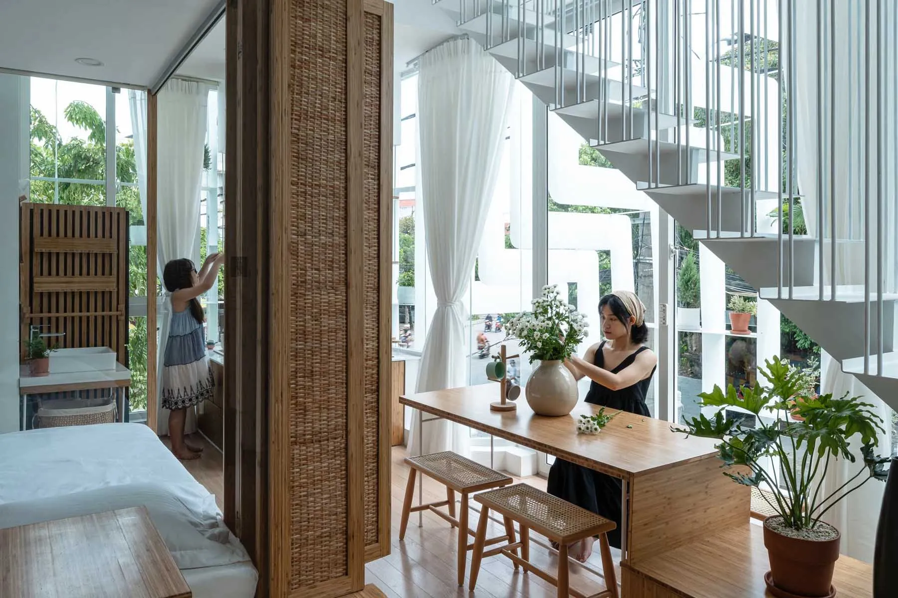 A modern apartment featuring woven fiber blinds, wooden stools, and a white bed.