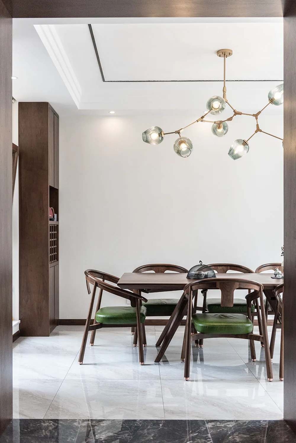 A modern dining room with a wooden table and green leather chairs.