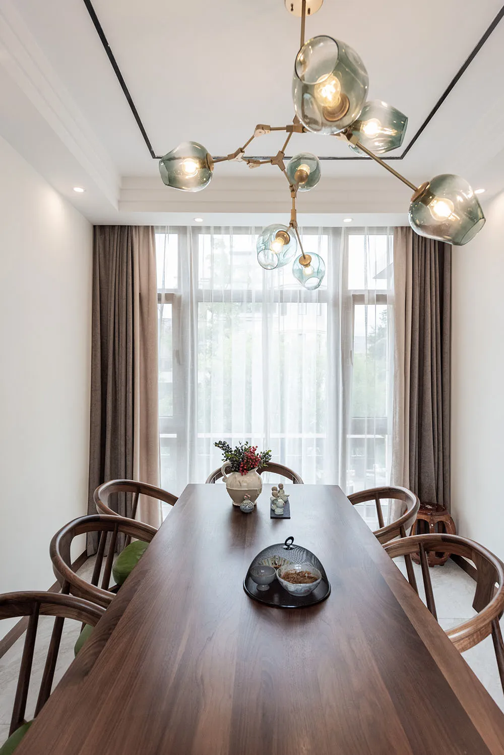 A modern dining room with a wooden table, green cushions, and a chandelier.