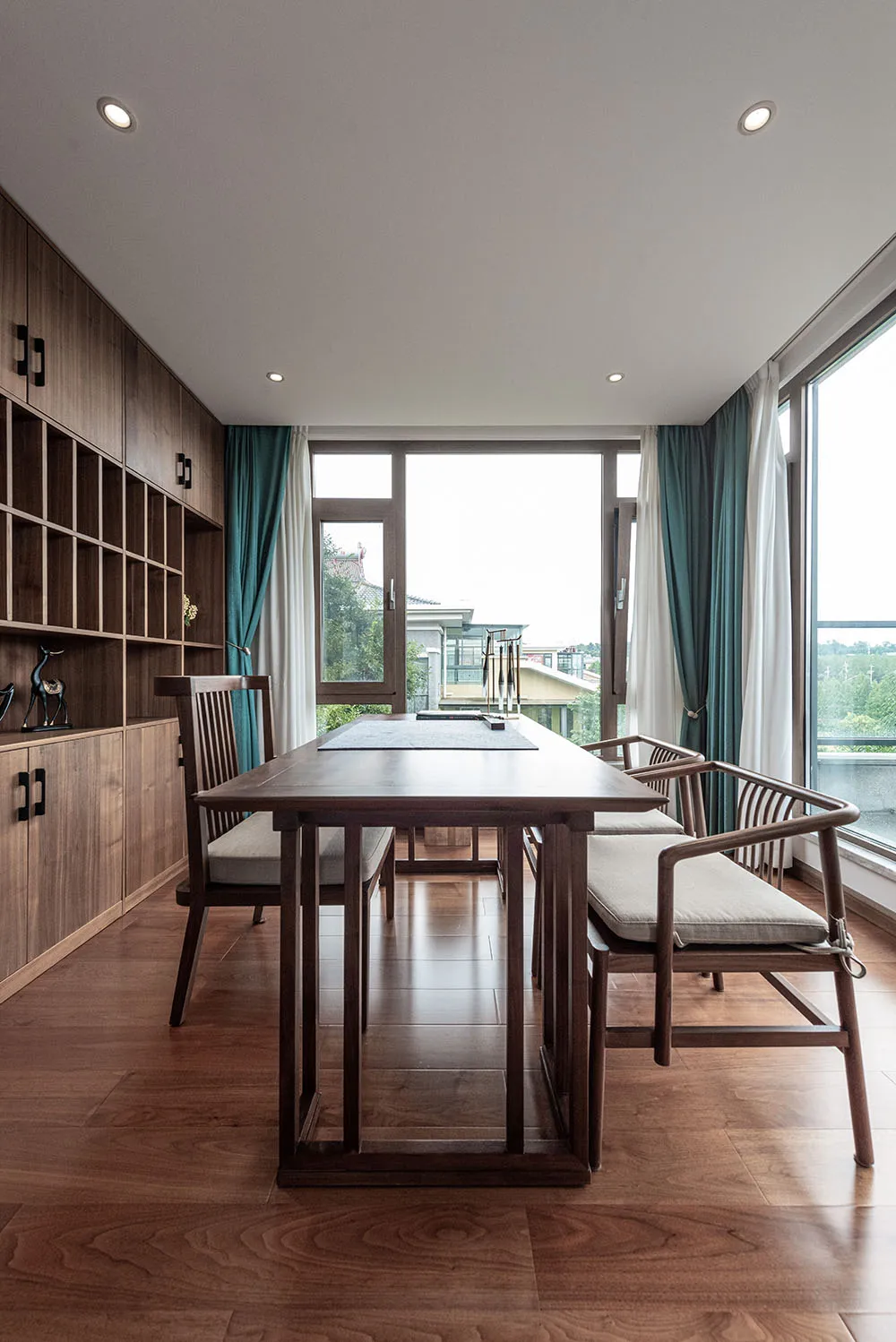 A modern dining room featuring a wooden table and chairs, with a large window and green curtains.