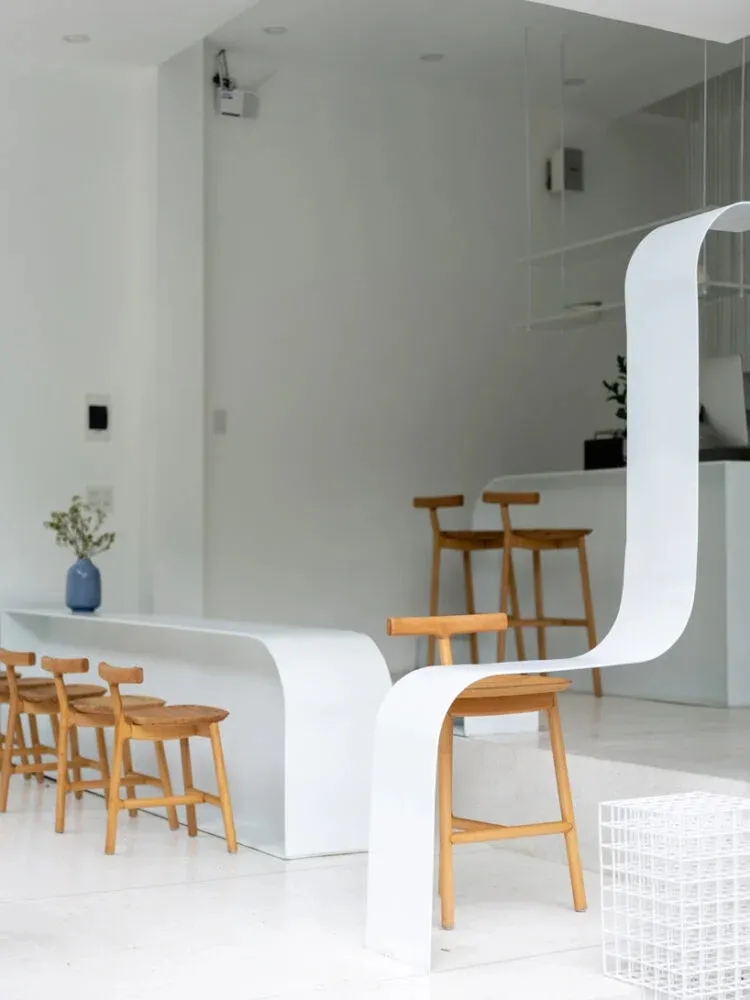 A modern and minimalist coffee shop with wooden stools and white surroundings.