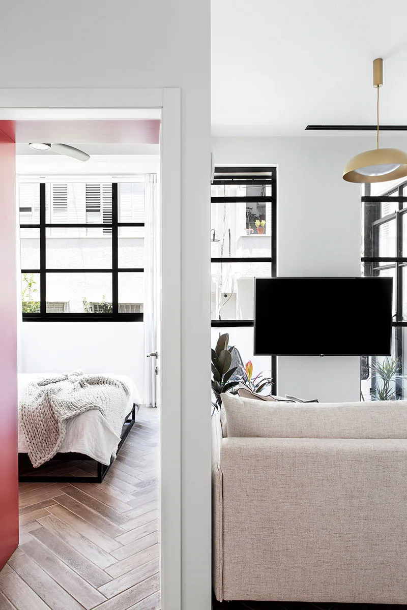 A minimalist living room with a neutral-toned sofa, a mounted TV, and herringbone-patterned flooring.