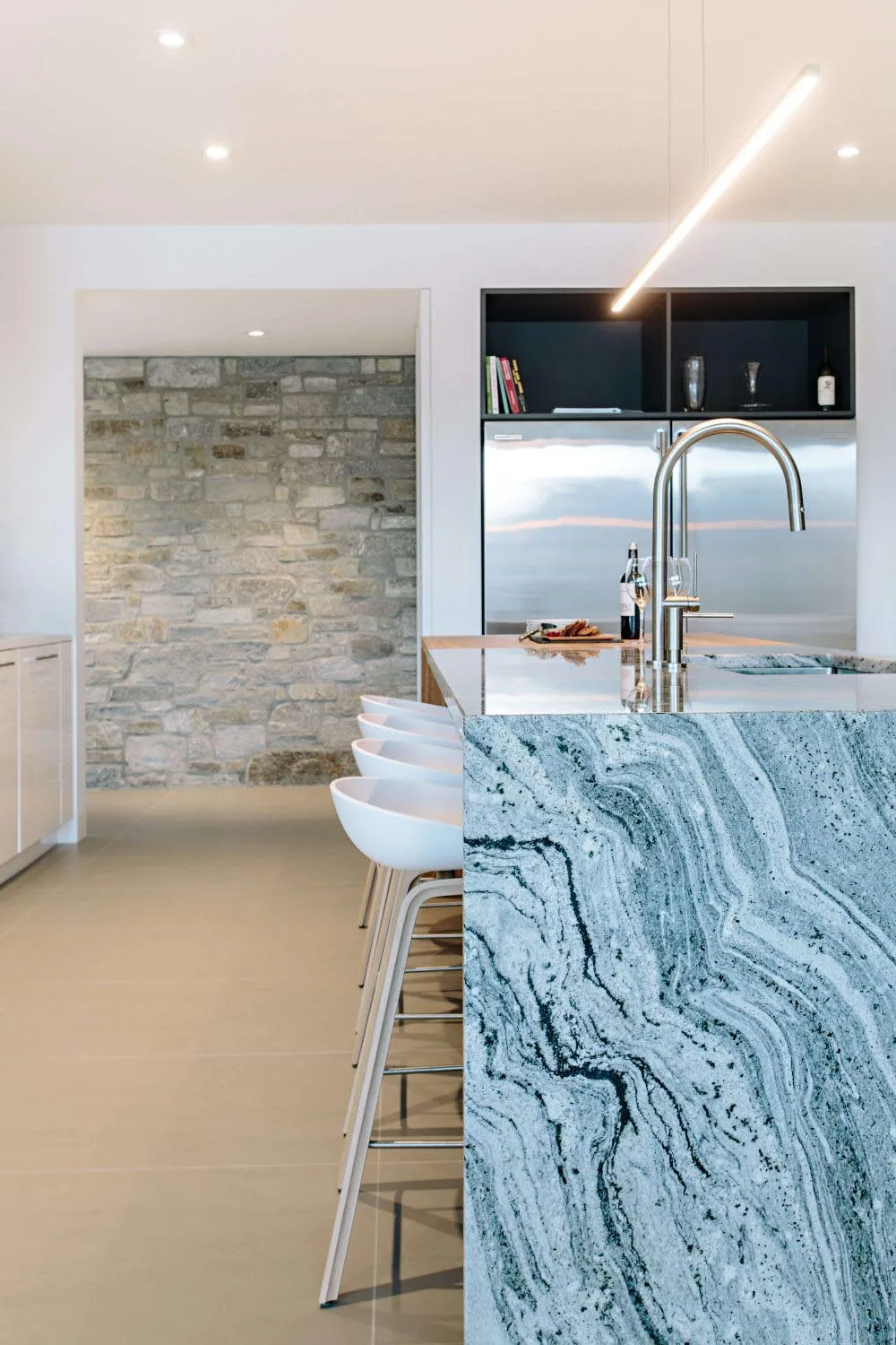 Modern minimalist kitchen featuring a sleek granite countertop and white stools.