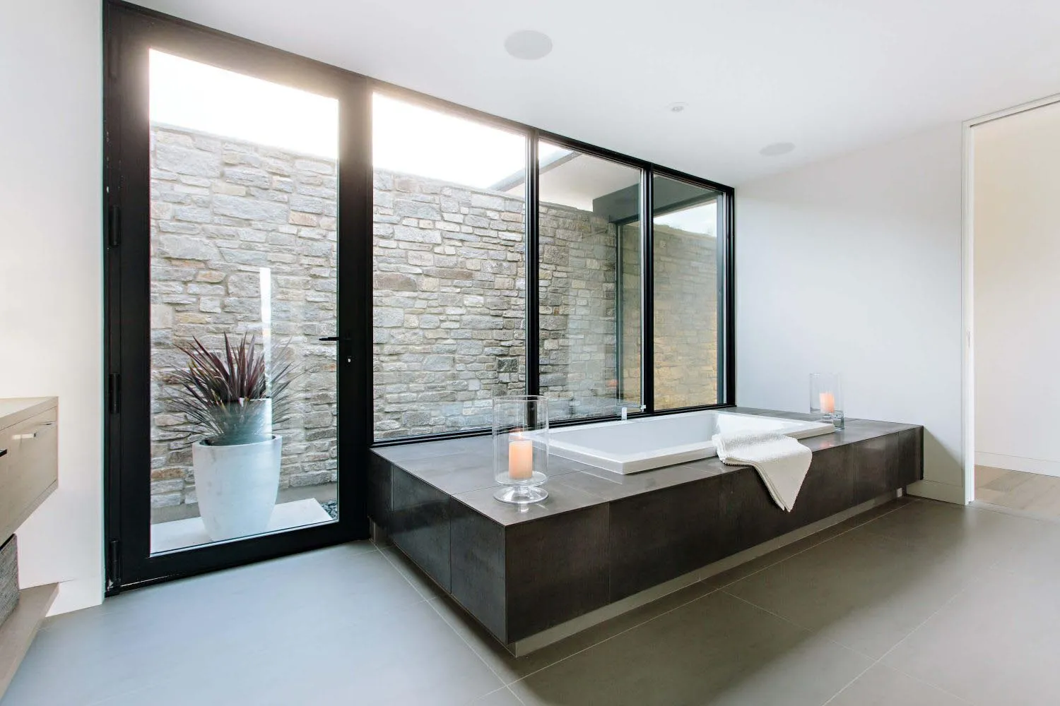 A modern bathroom featuring a walk-in shower with glass windows, a minimalist tub, and a stone wall background.
