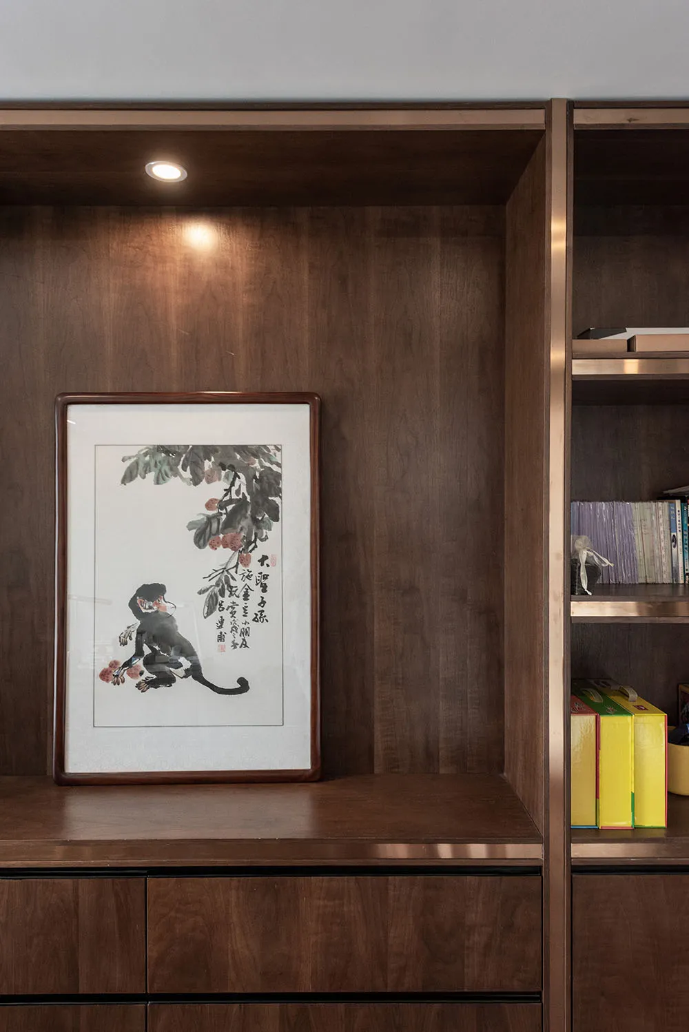 A wooden bookshelf with a framed painting of a monkey and flowers on it.