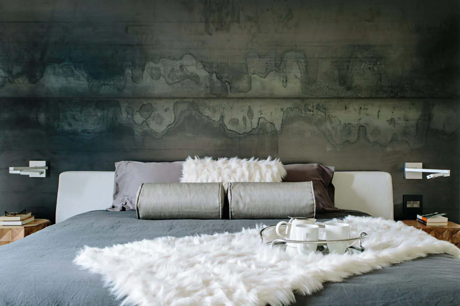 A minimalist bedroom with a faux concrete headboard and a plush white wool blanket, featuring modern and sleek design element
