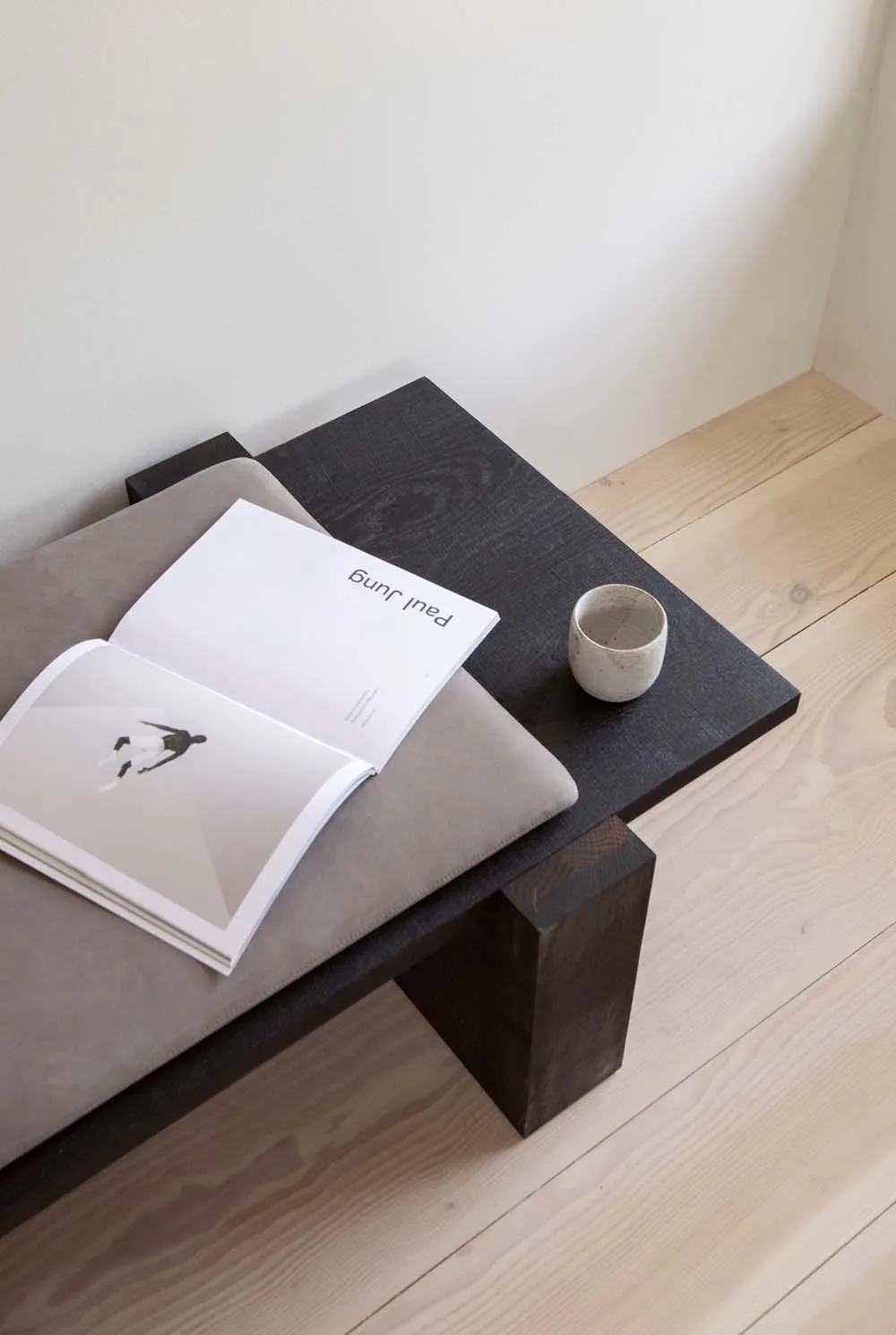 A minimalist interior with a black wooden coffee table, an open book, and a ceramic cup.