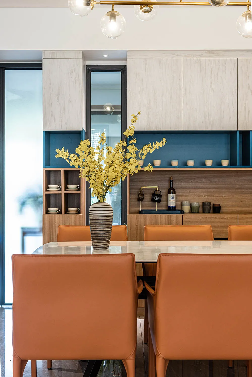 A modern dining room featuring wooden furniture and glass elements, with a vase of yellow flowers on the table.