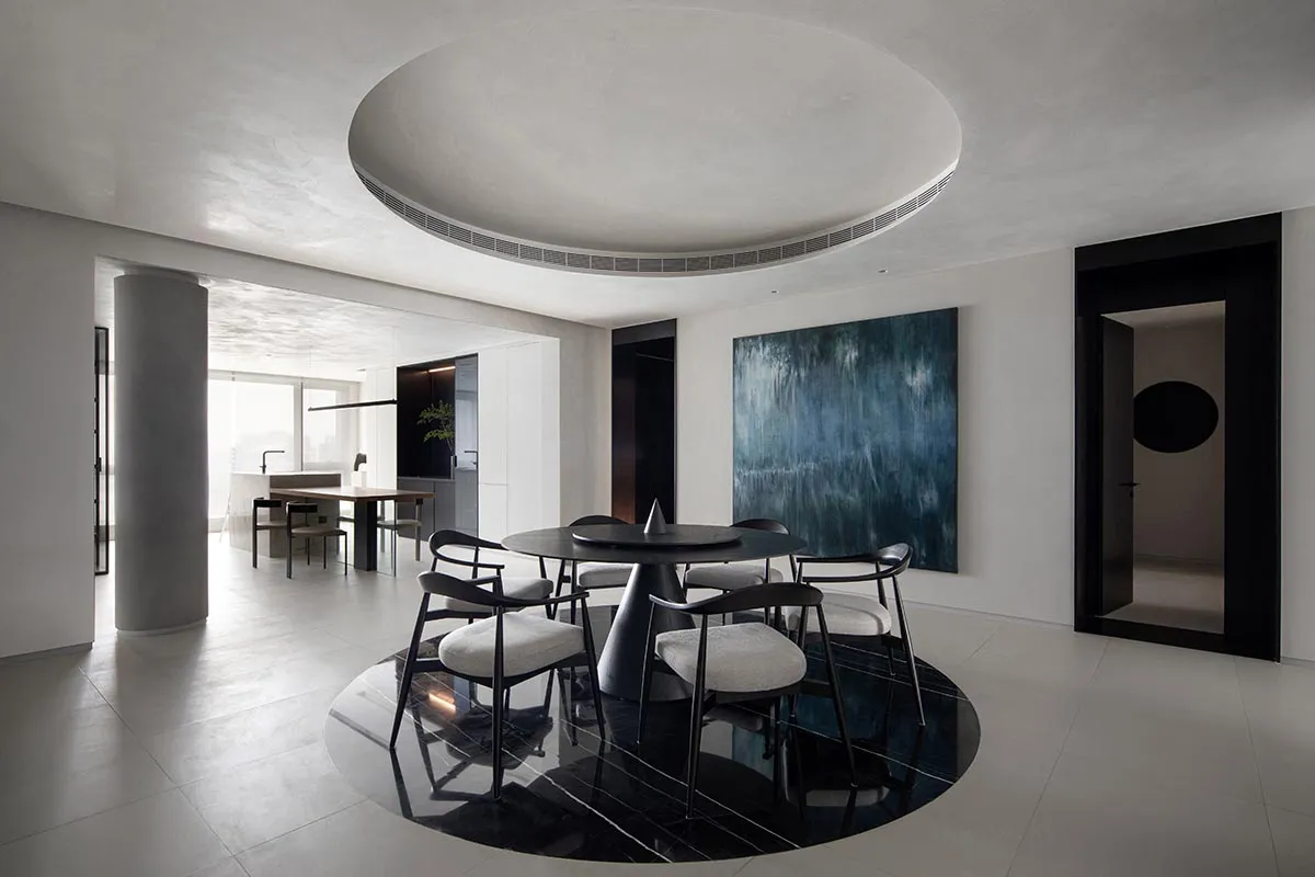 Circular modern interior featuring a black marble dining table with white chairs, white walls, and a large blue abstract pain