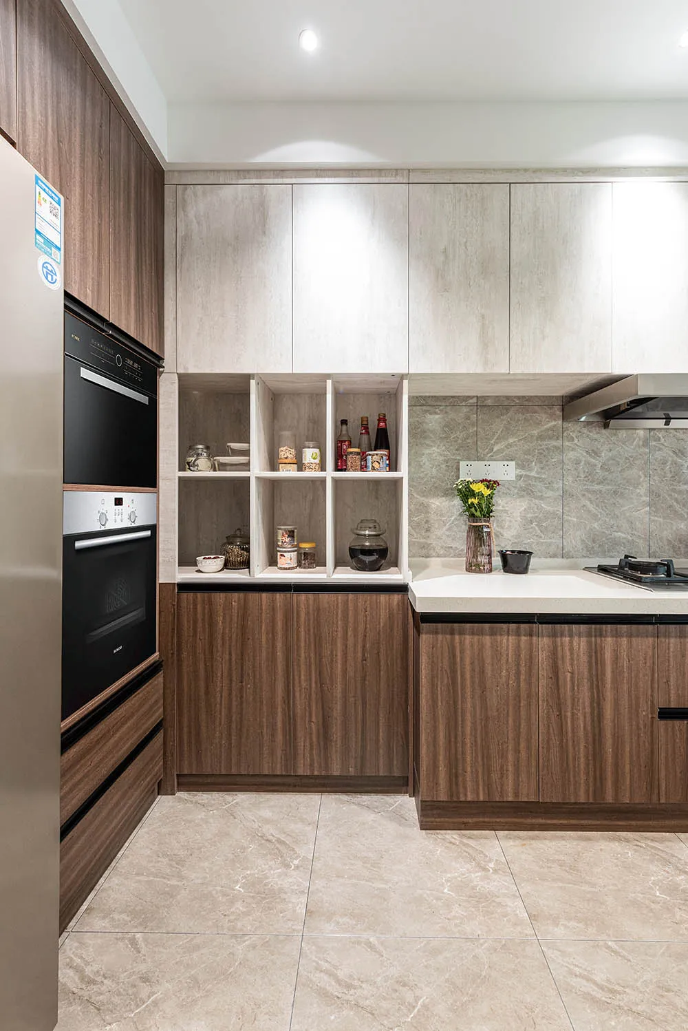 Modern kitchen featuring wooden cabinets and a marble countertop with assorted jars and bottles on open shelves and a stainle