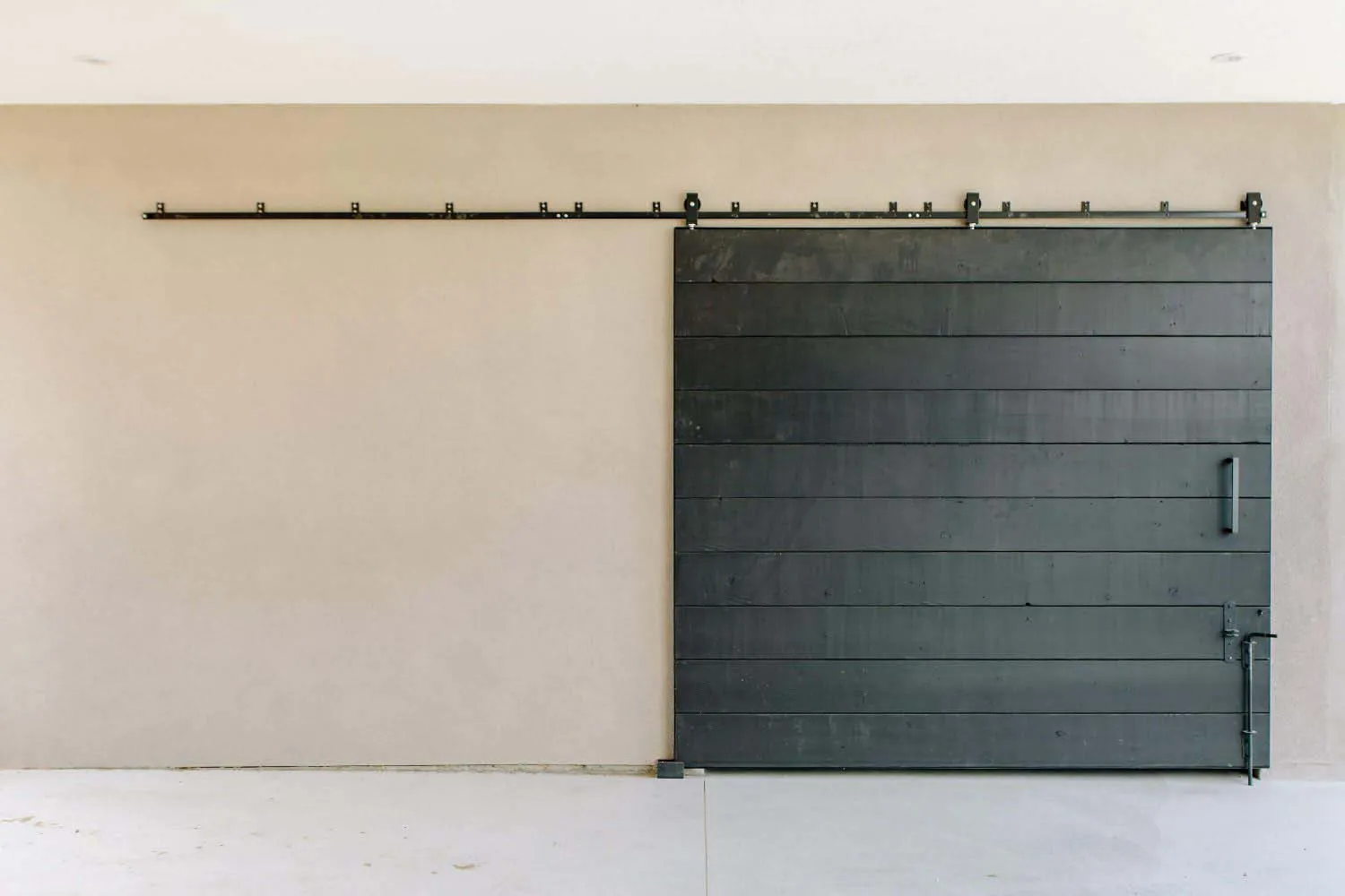 A modern, minimalist barn door wall featuring a horizontal black slat wall on a beige wall with a black metal rail mounted ab