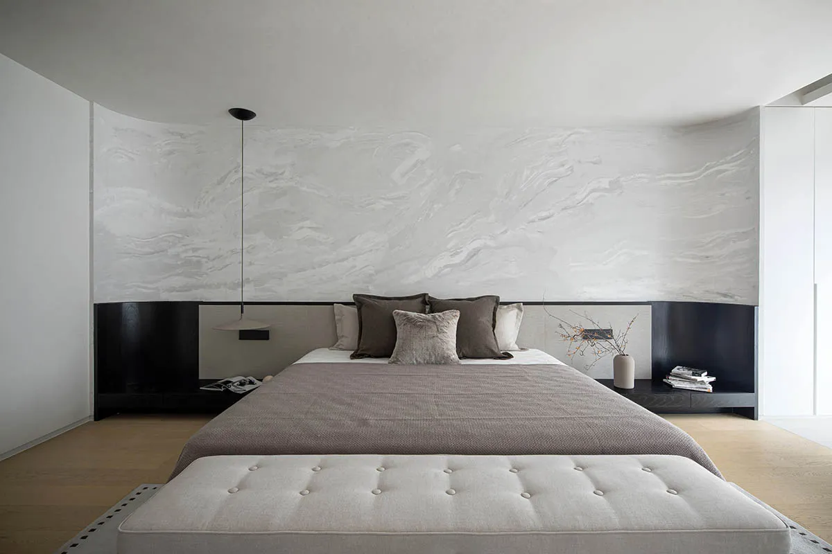 A minimalist bedroom with a marble-patterned wall, a large bed, and a tufted bench.