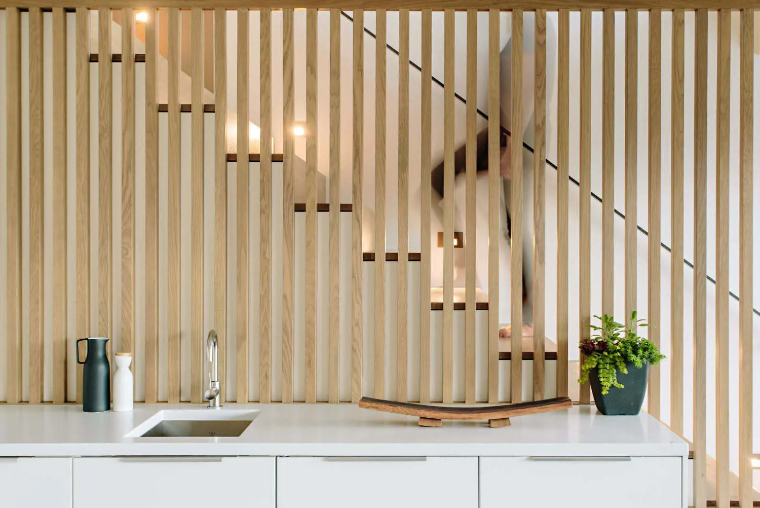 Modern minimalist interior with wooden panel wall and white kitchen counter with sink.