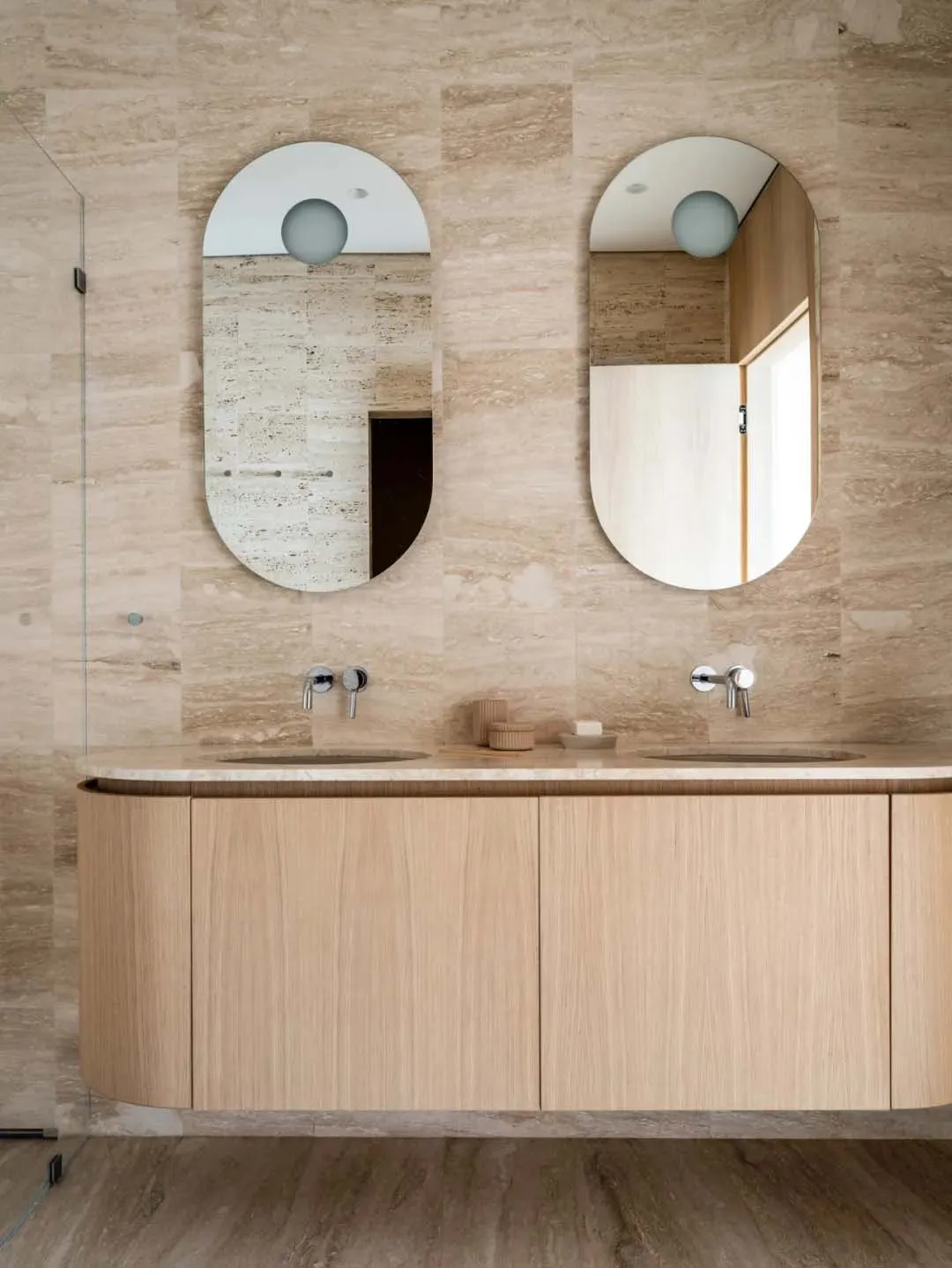 A modern bathroom featuring oval mirrors and double sinks with a natural stone and wood vanity.