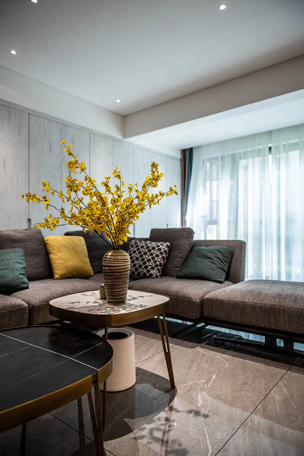 Modern living room with a gray sectional sofa, yellow flowers in a vase, and marble coffee table.