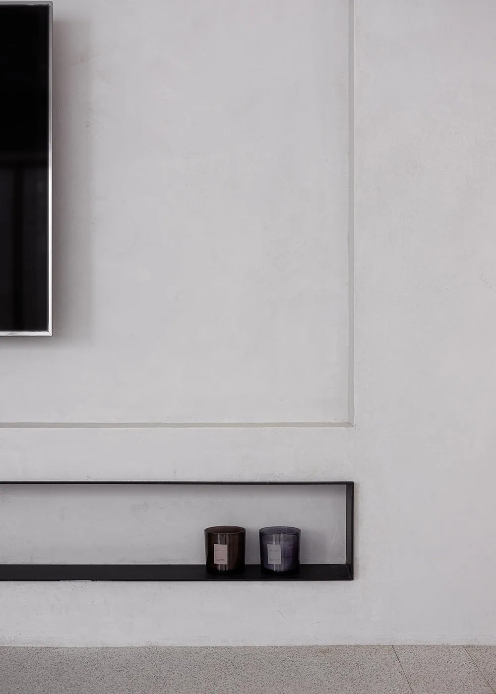 A minimalist interior with a concrete floating shelf holding two candles.