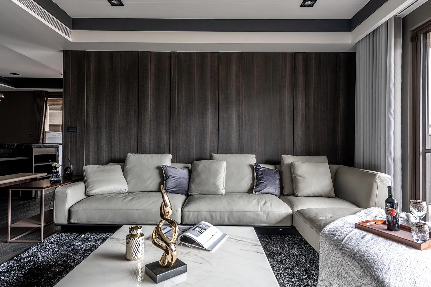 Modern living room with a grey leather sofa, wooden accent wall, and a marble coffee table with decorative items.