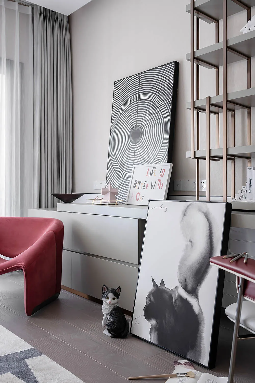 A modern living room featuring minimalist art, a red armchair, and a grey cat statue.