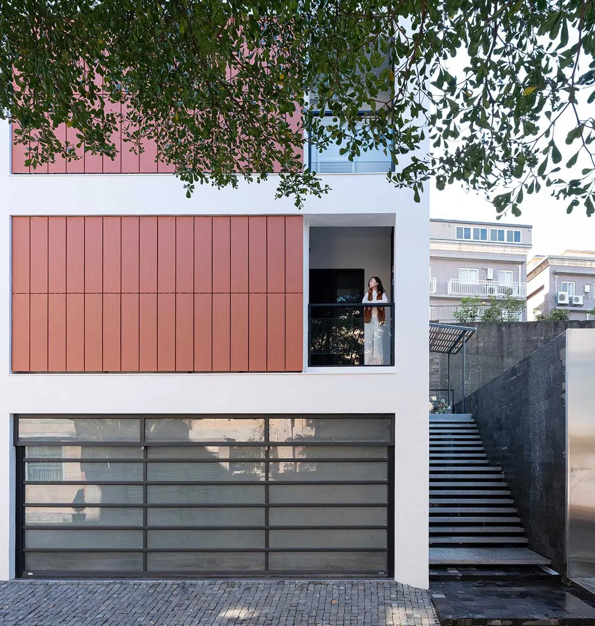 Modern residential building with metal and glass façade, concrete steps, and a woman looking out a window.