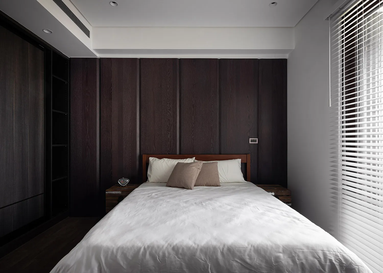 A minimalist bedroom with wooden paneling, white bedding, and two pillows.