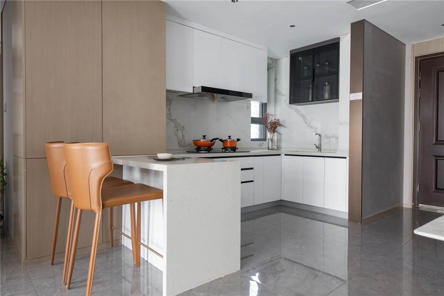 Modern kitchen with marble countertops, white cabinets, and orange pots on the stove.