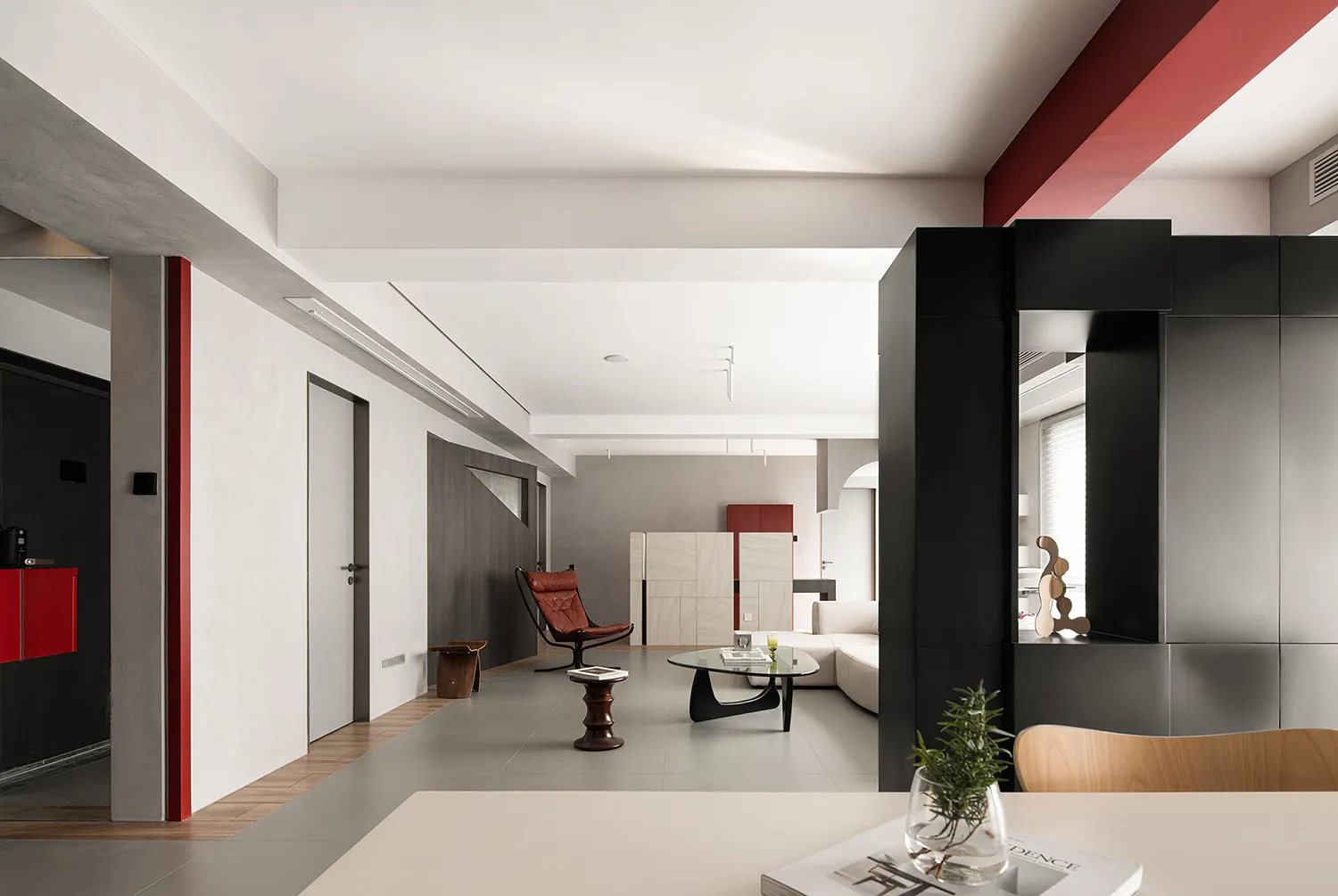 Minimalist living room with concrete walls, red accents, and modern furniture.