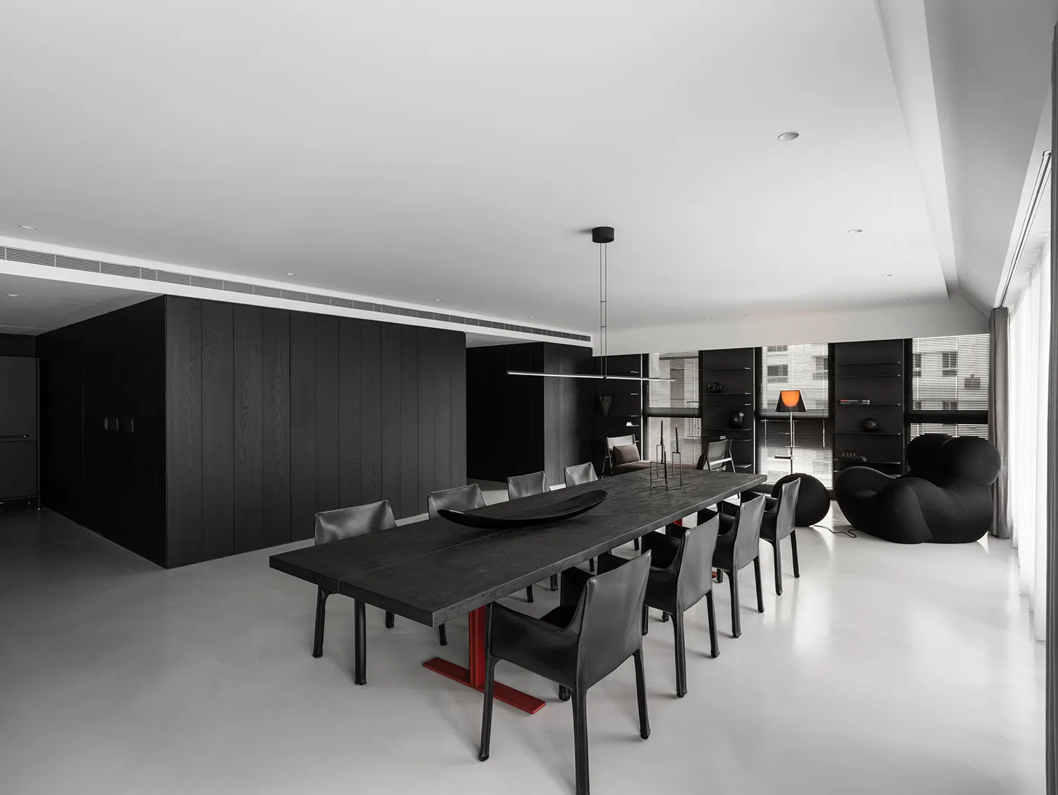A minimalist dining room with a long, dark table and black chairs against a white floor and black wooden walls.