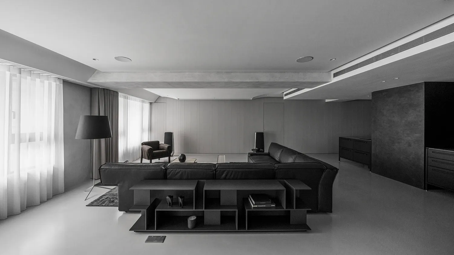 A minimalist living room with black furniture, concrete walls, and a large floor lamp.