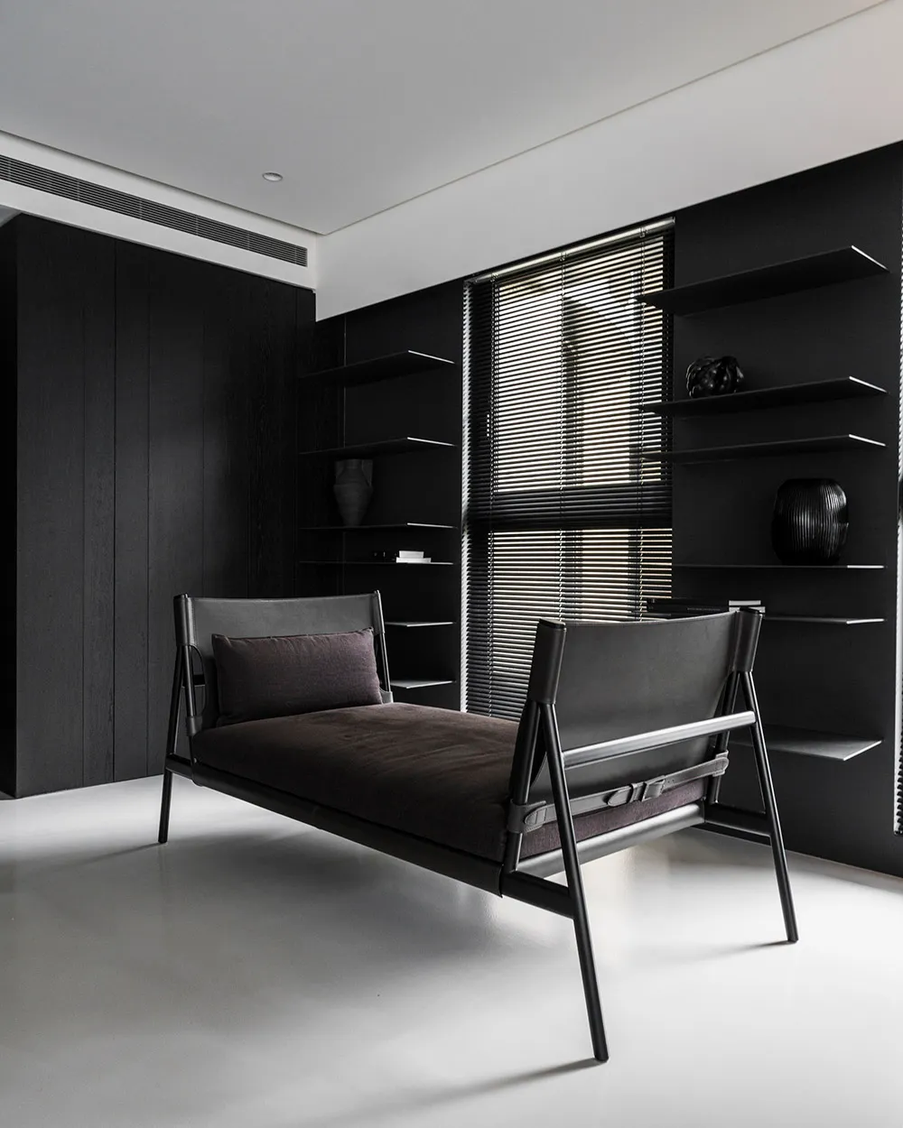 A minimalist bedroom with a black metal frame bed, black shelving, and a contrasting white floor.