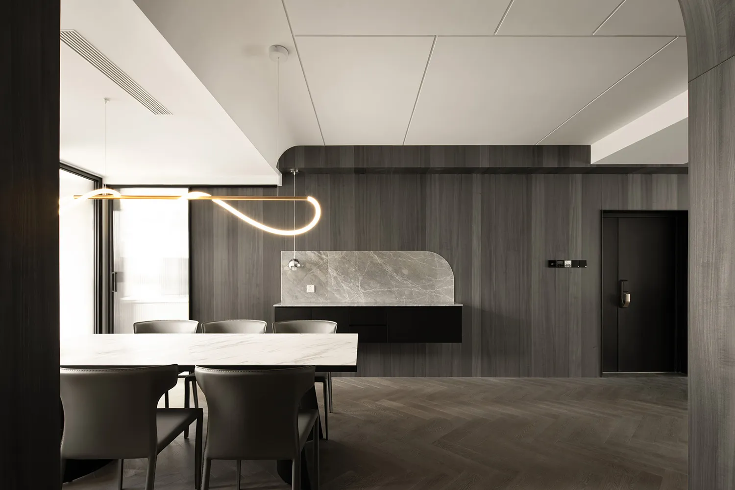 Contemporary kitchen with marble countertops and dark wooden walls, featuring a unique pendant light fixture.